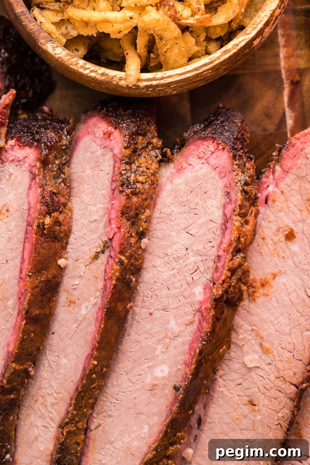 Sliced smoked brisket with a dark crust next to a bowl of crispy fried onions.