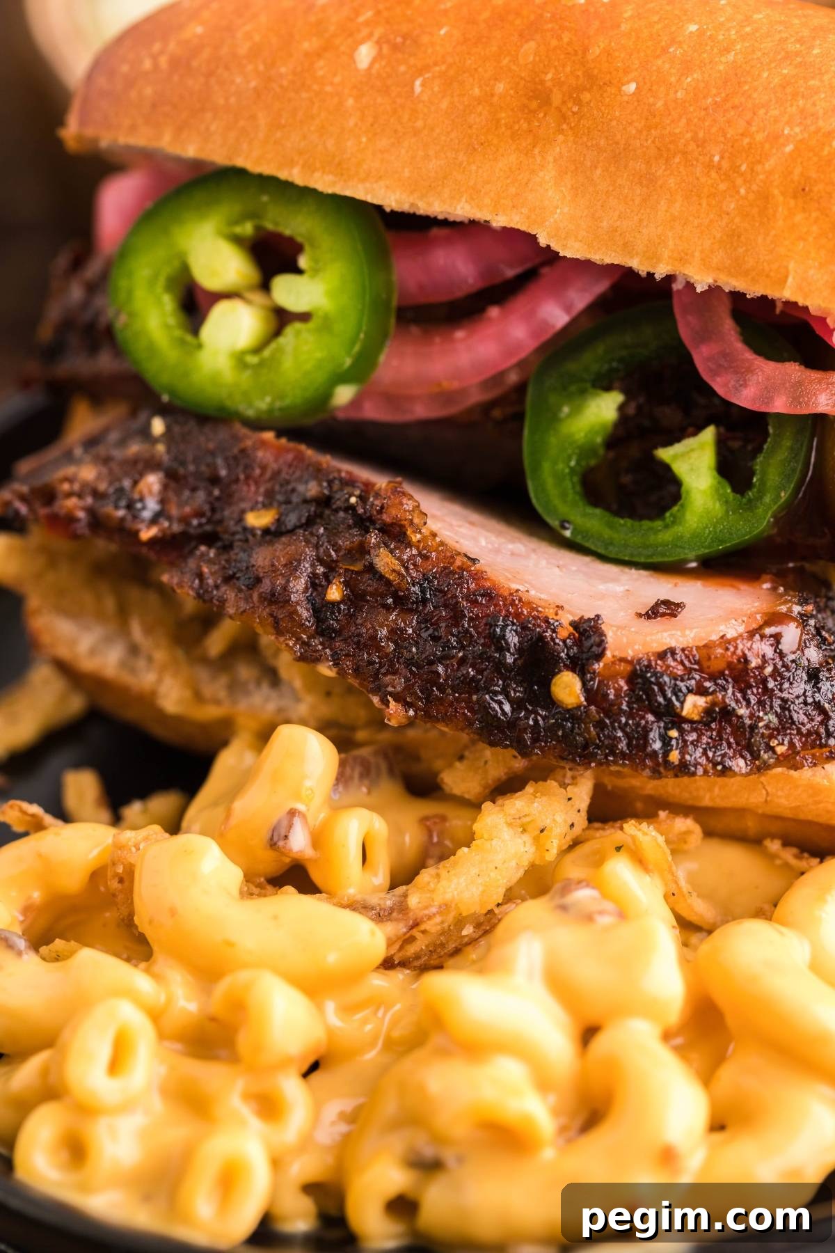 Close-up of a brisket sandwich stacked with pickled onions and jalapeños, served with mac and cheese.