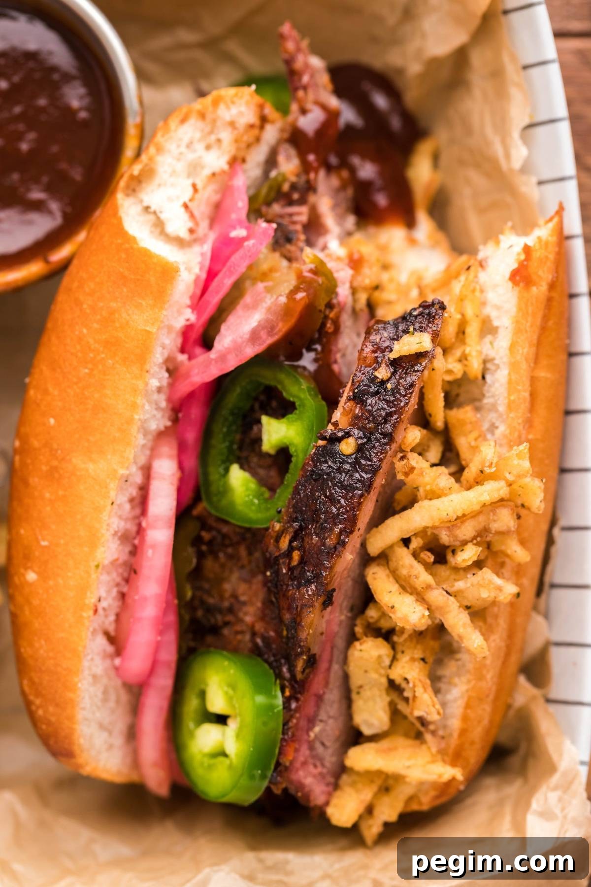 Smoked brisket sandwich with pickled onions, jalapeños, crispy onions and sauce on a hoagie roll.