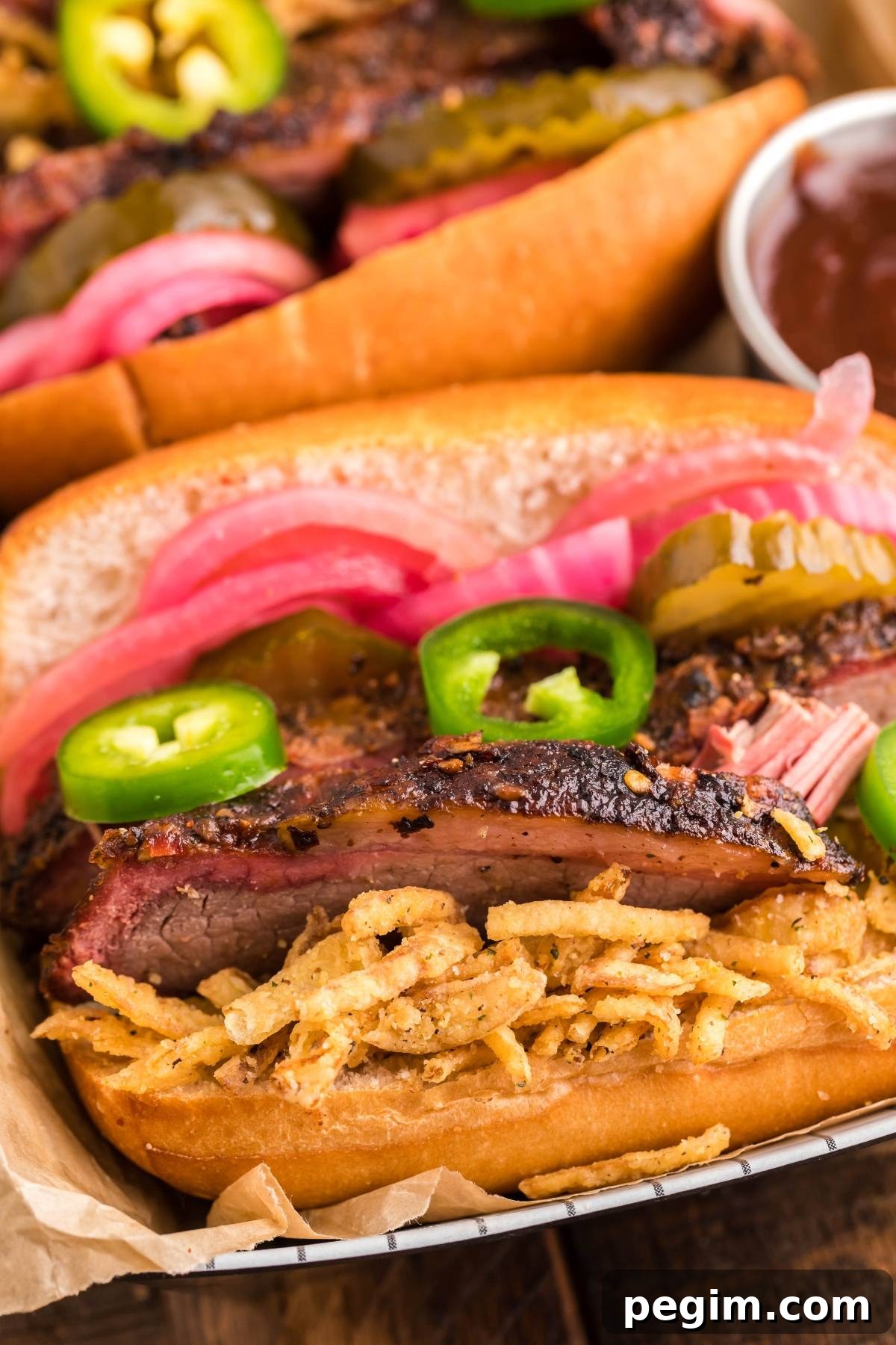Smoked brisket sandwich stacked with pickled onions, jalapeños and crispy onions in a toasted bun.