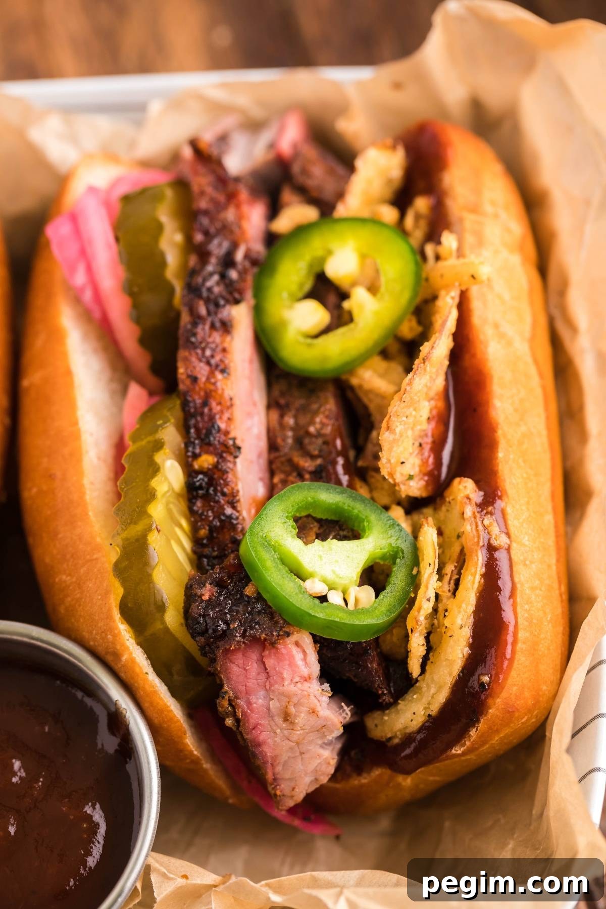 Smoked brisket sandwich piled high with sliced brisket, pickles, crispy onions and jalapeños on a fresh bun.