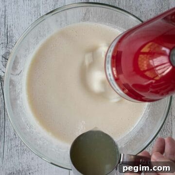 Adding lemon juice to beaten eggs and sugar using red hand held electric mixer.