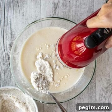 Adding flour to beaten eggs and sugar using a red hand held electric mixer.