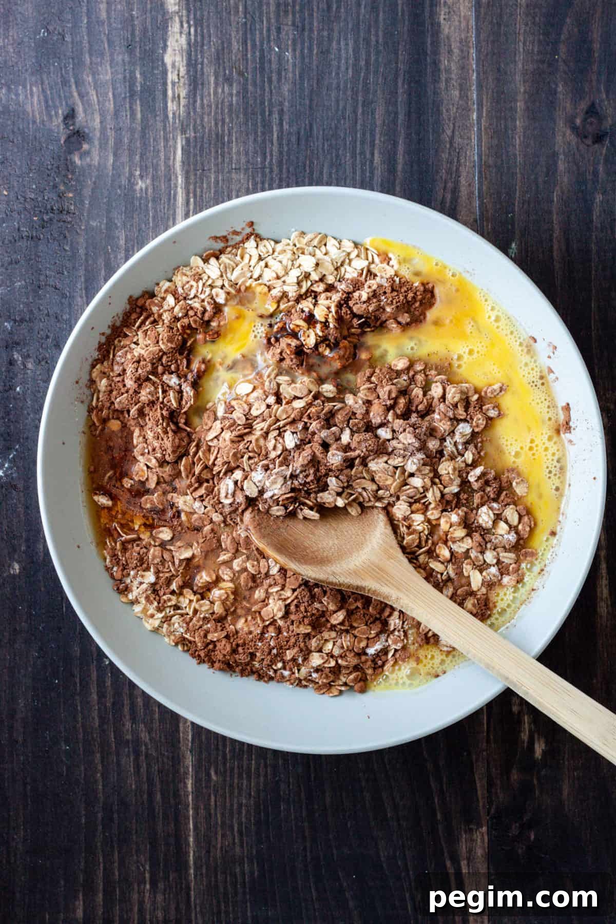 Chocolate baked oatmeal getting stirred together in a medium bowl with a wooden spoon.