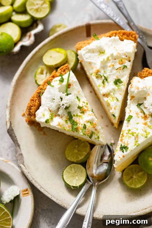 sliced key lime pie on a ceramic plate with fresh key limes, edible flowers, and serving spoons.