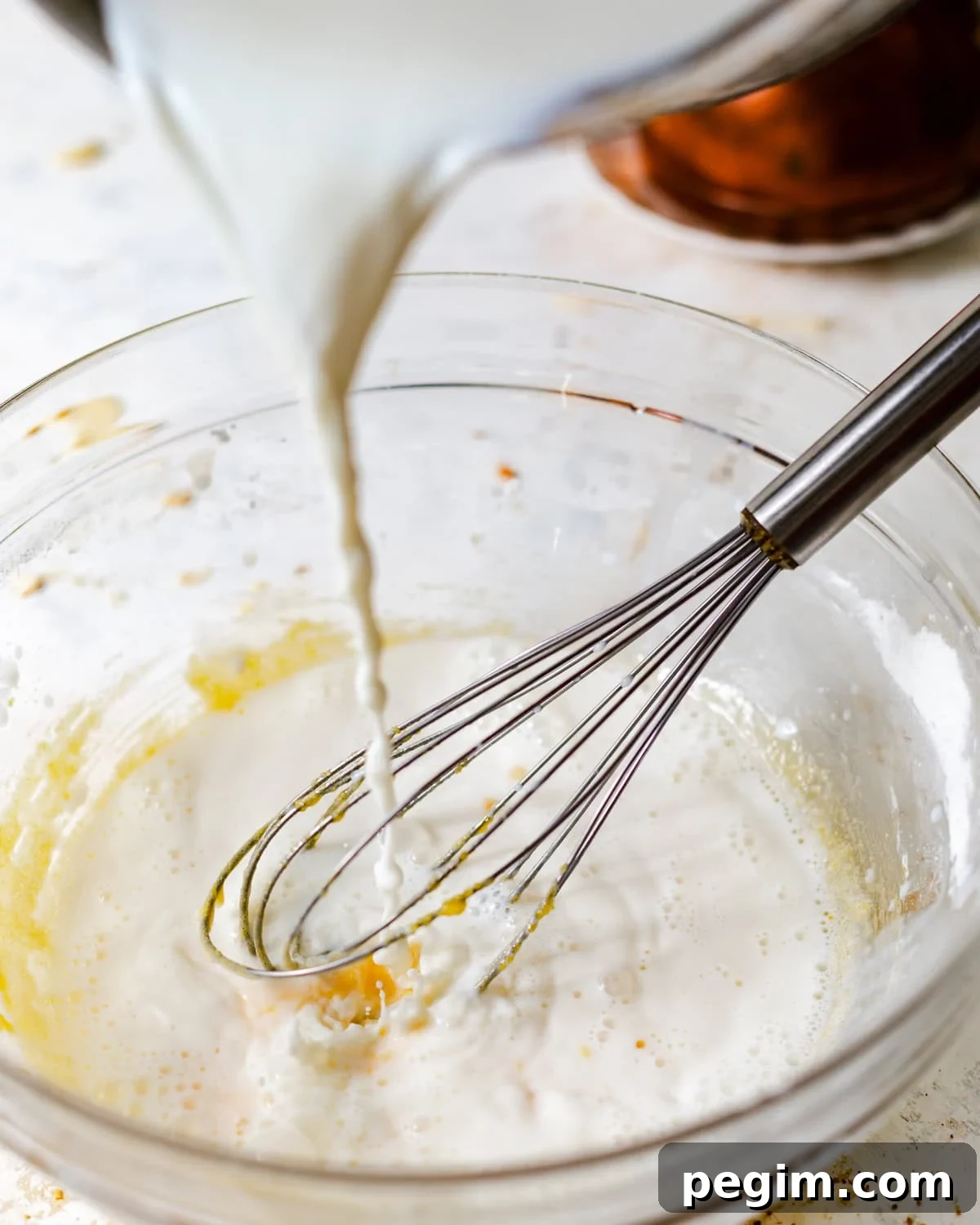 pouring warm milk into the egg yolk mixture while whisking.
