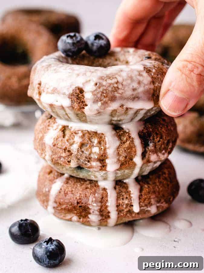Stack of 3 blueberry glazed cake donuts, hand reaching for top one
