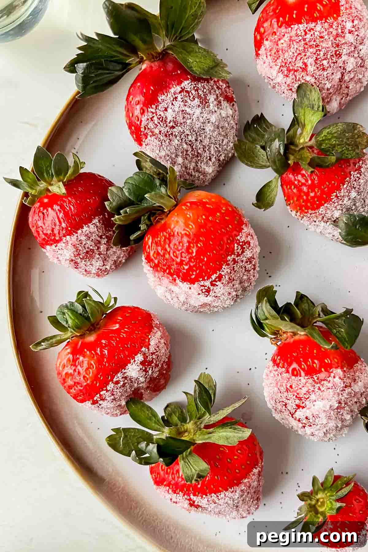 champagne soaked strawberries dipped in sugar aligned on white plate.