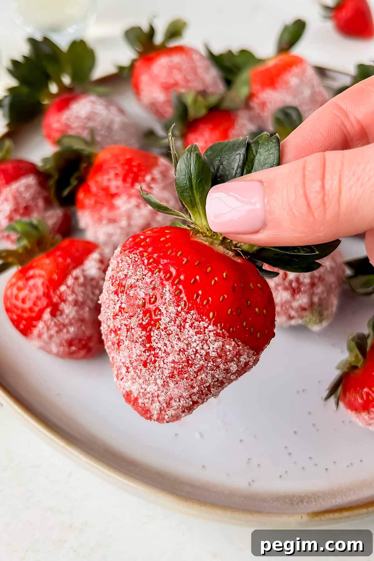 hand grabbing champagne soaked strawberry dipped in sugar.