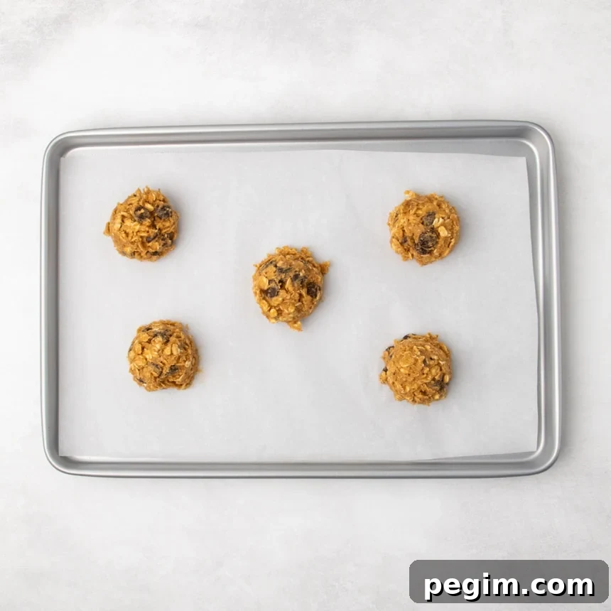 A parchment-lined metal baking sheet with five portions of oatmeal cookie dough spaced evenly apart.
