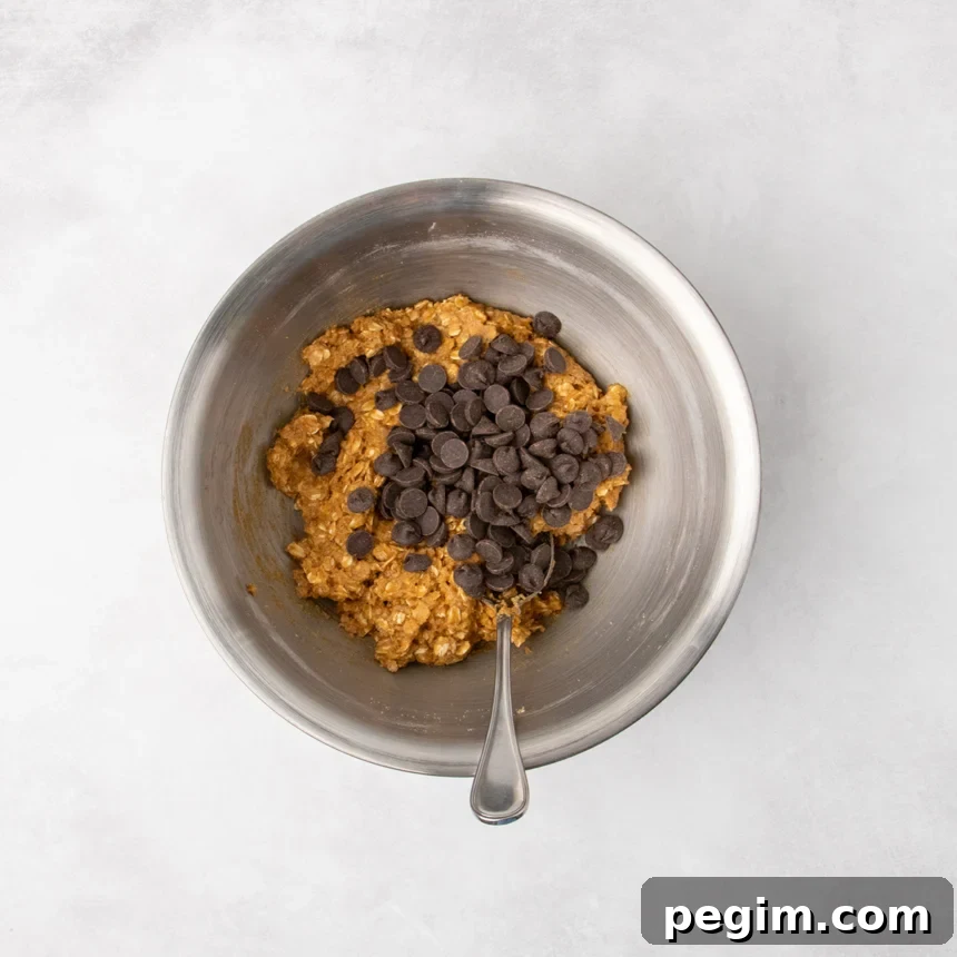 The same metal mixing bowl with the same cookie dough and dark chocolate chips added on top, with a spoon resting in the bowl.