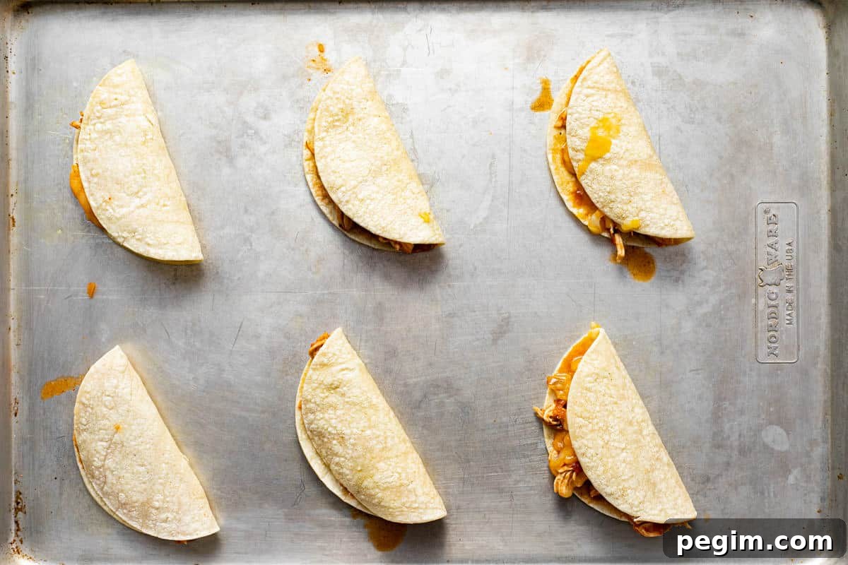Metal baking sheet with unbaked mini chicken tacos.