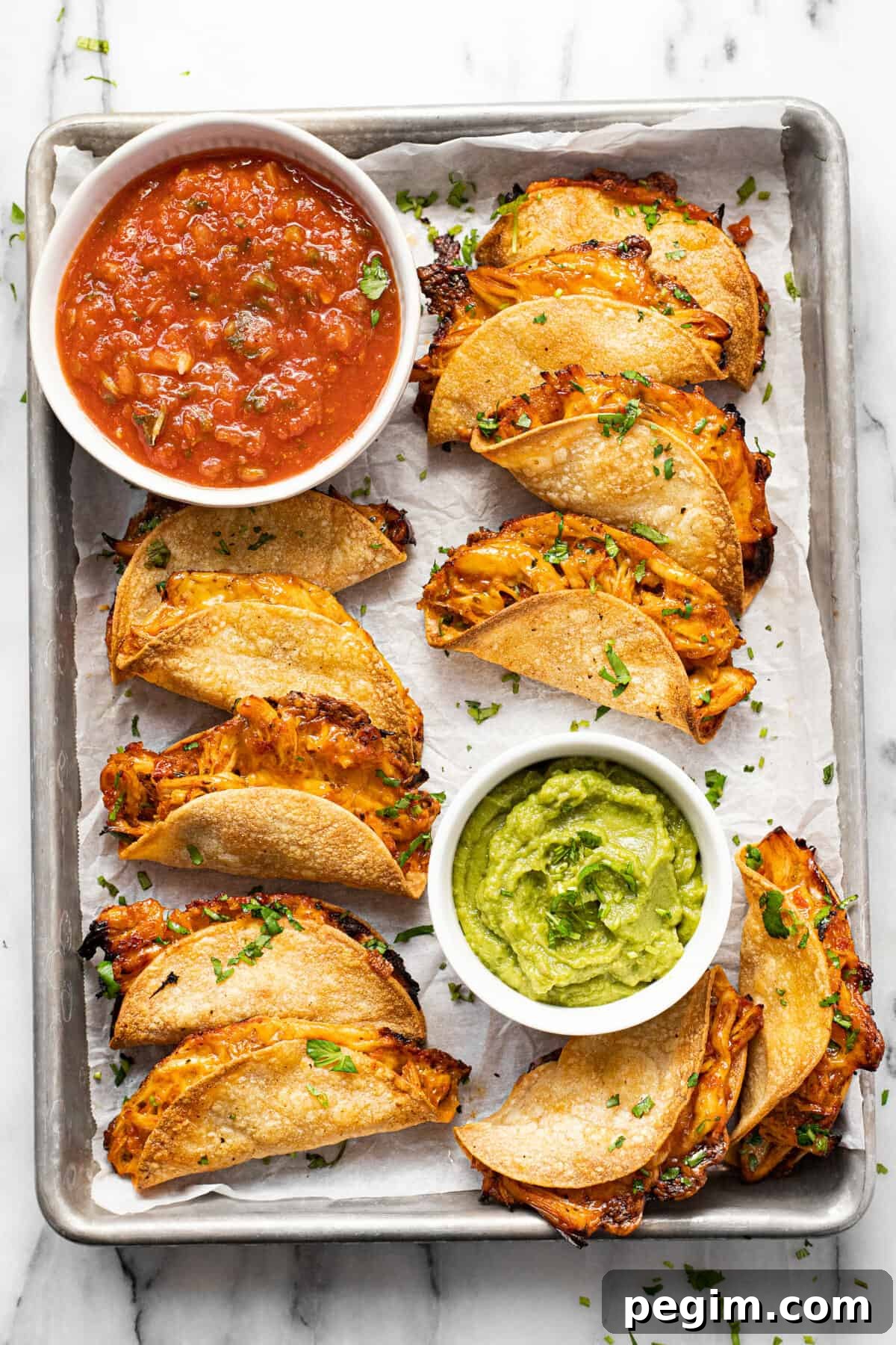 Parchment lined baking sheet filled with mini tacos, guacamole, and salsa.