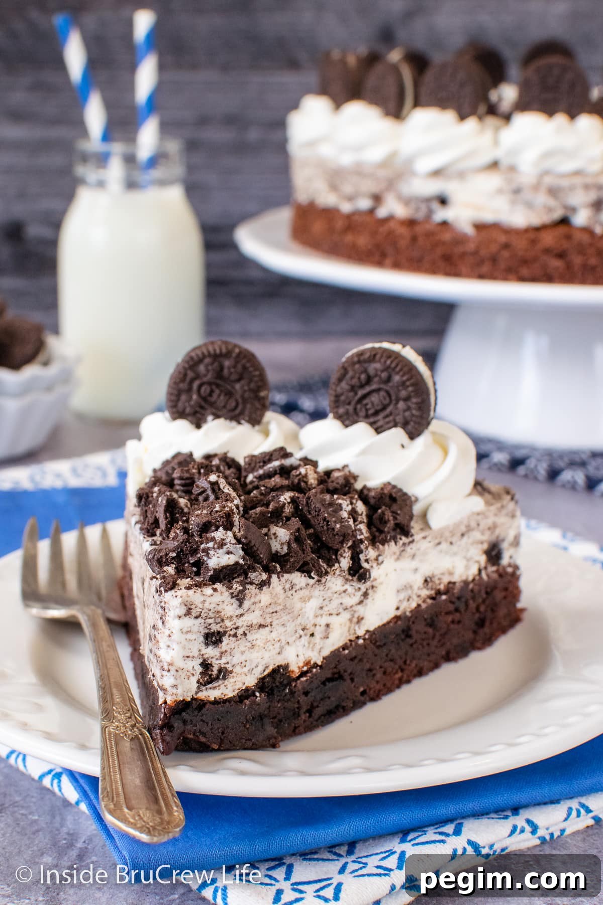 A slice of Oreo mousse cake on a white plate topped with Cool Whip and Oreo cookie chunks.