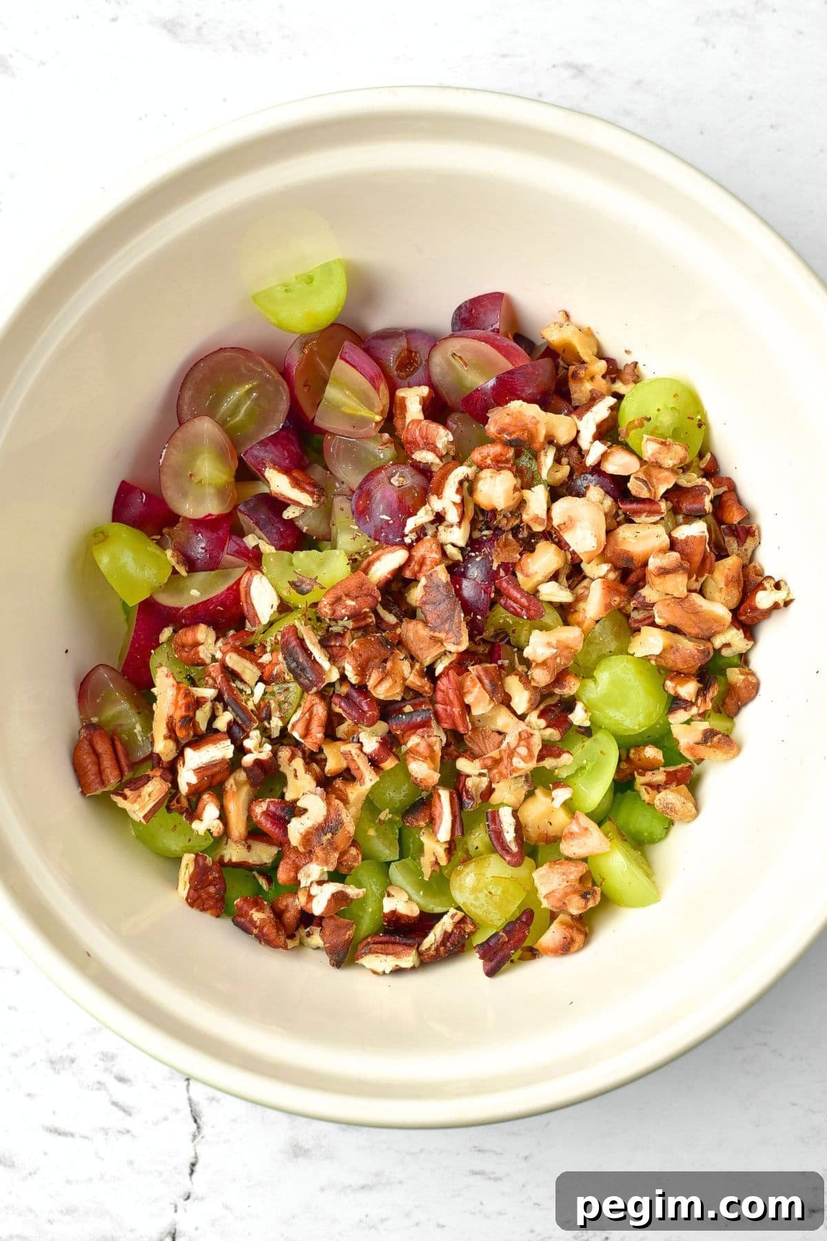 Chopped nuts, sliced grapes and chopped celery in white bowl.