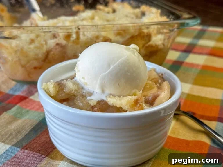 Warm apple crisp with a sweet and easy topping and a simple sauce with vanilla ice cream melting on top on a plaid napkin.