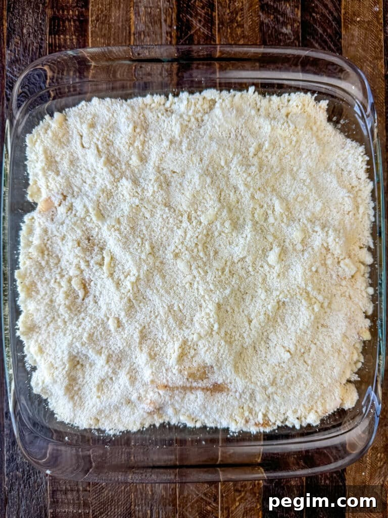 Simple topping without oats spread over a dish of apple crisp ready to bake.