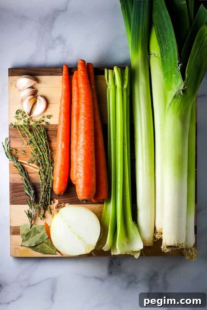 Carrots, leeks, celery, garlic and herbs unchopped, on a wooden cutting board
