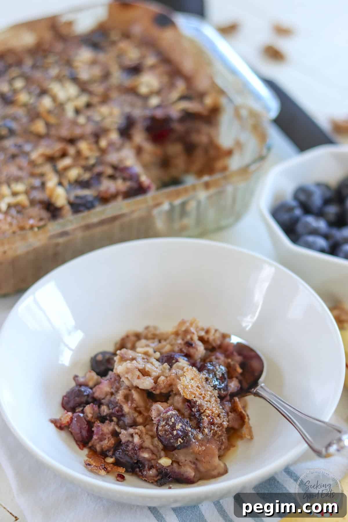 A square baking dish and a white bowl served with baked oatmeal and blueberries.