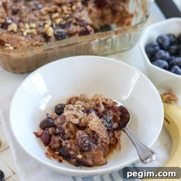 Blueberrry banana baked oatmeal in a white bowl with a bowl of blueberries in the background.
