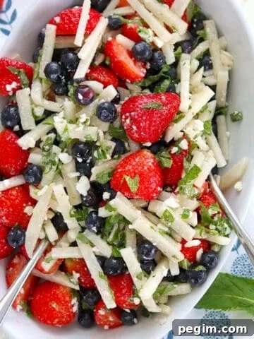 Serving a red white and blue fruit salad in a white oval bowl and two silver spoons.