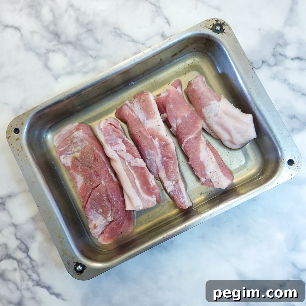 Pork belly slices arranged in apple juice in a metal roasting tray.