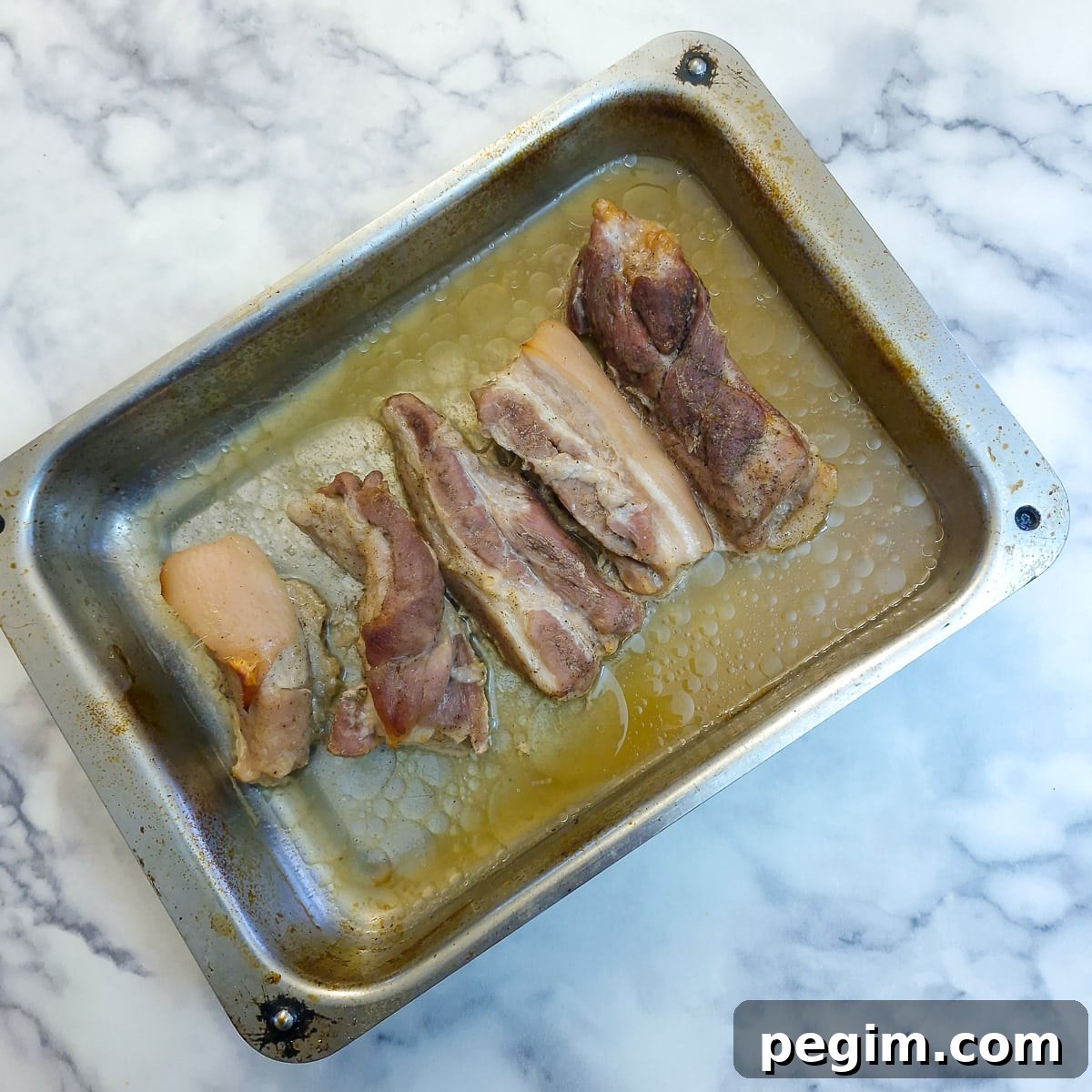 Cooked pork belly slices in the baking tray after fat has rendered out.
