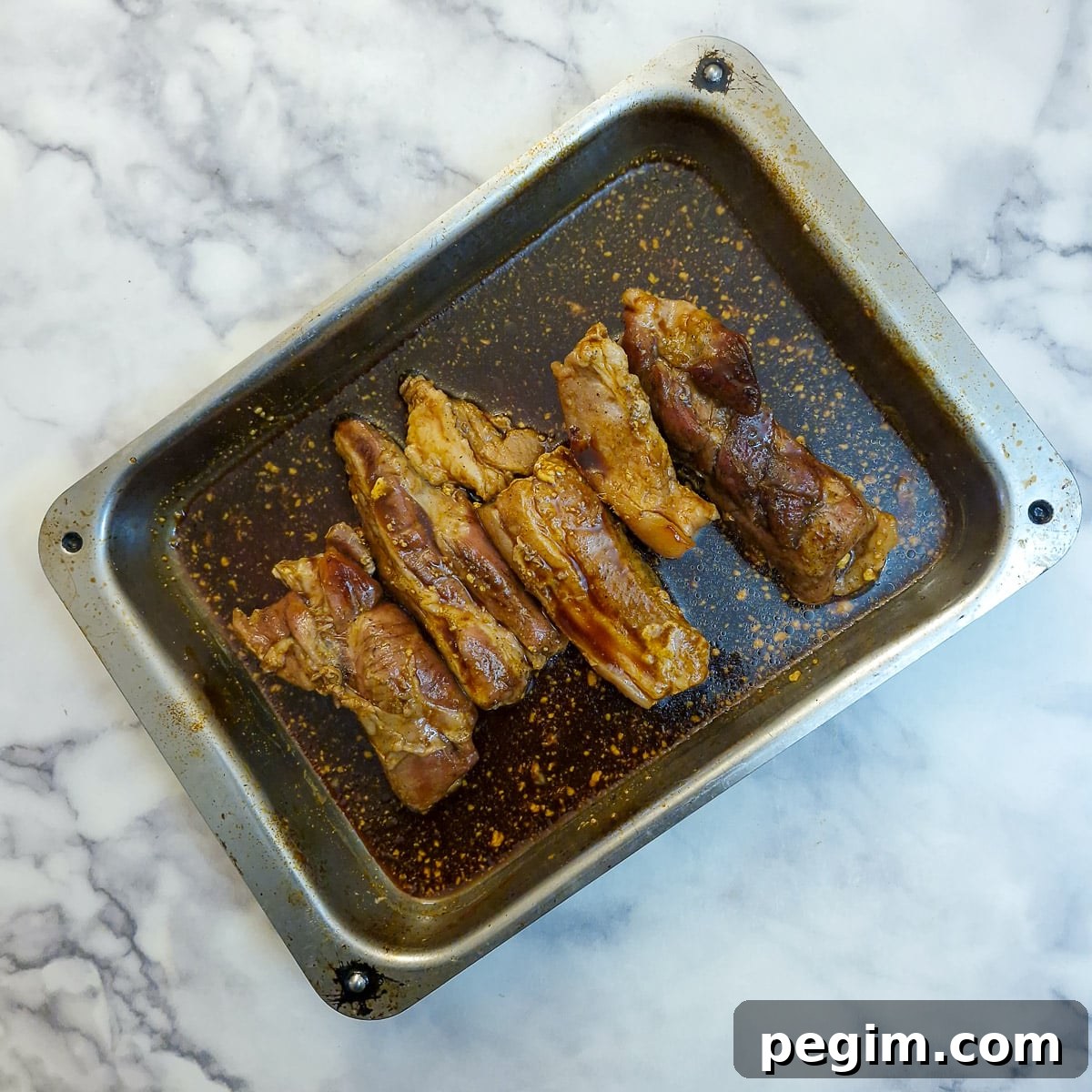 Pork belly slices coated in glaze in a roasting pan.