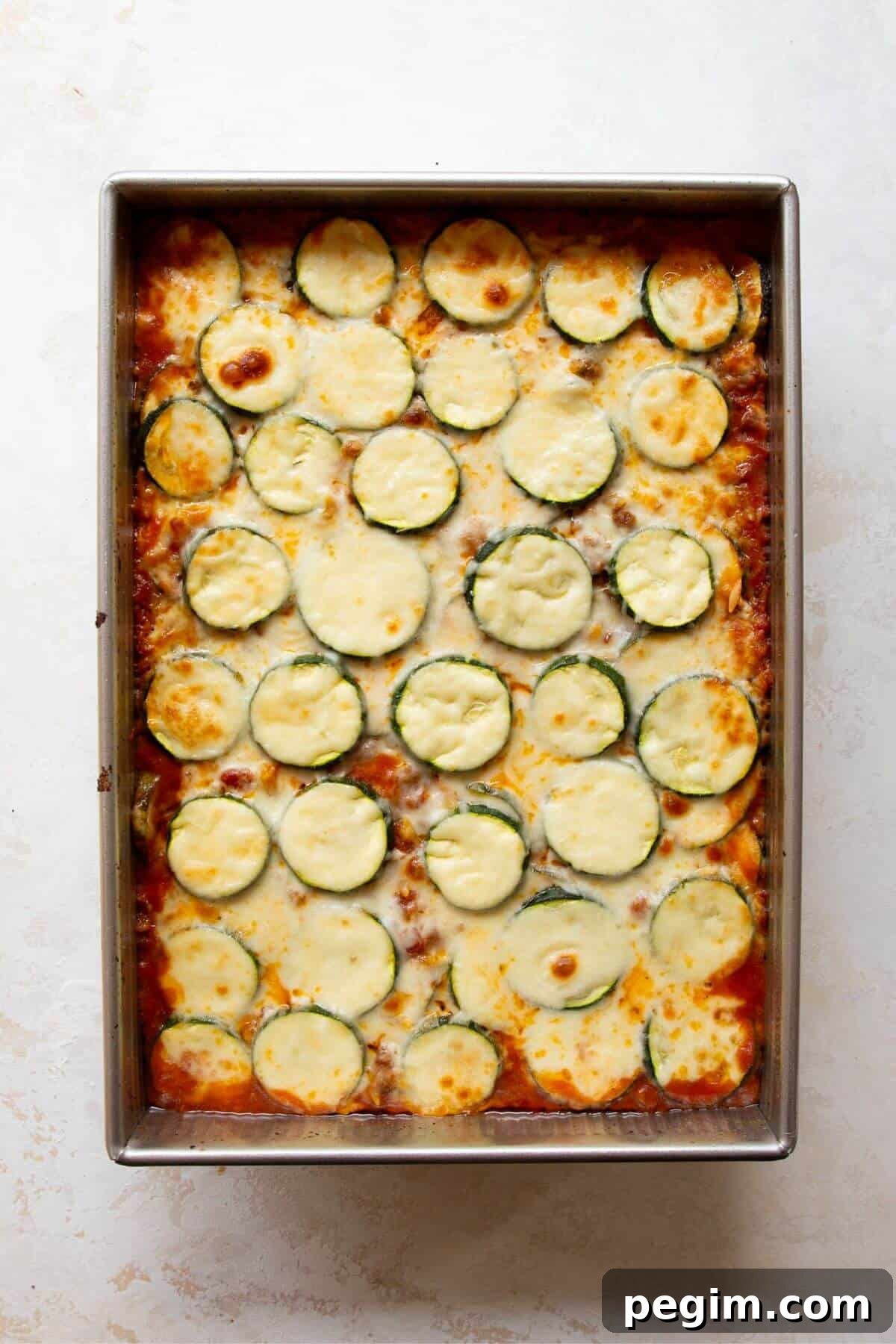 Baked ground beef and zucchini casserole in a dish fresh out of the oven with golden, gooey melted cheese on top.