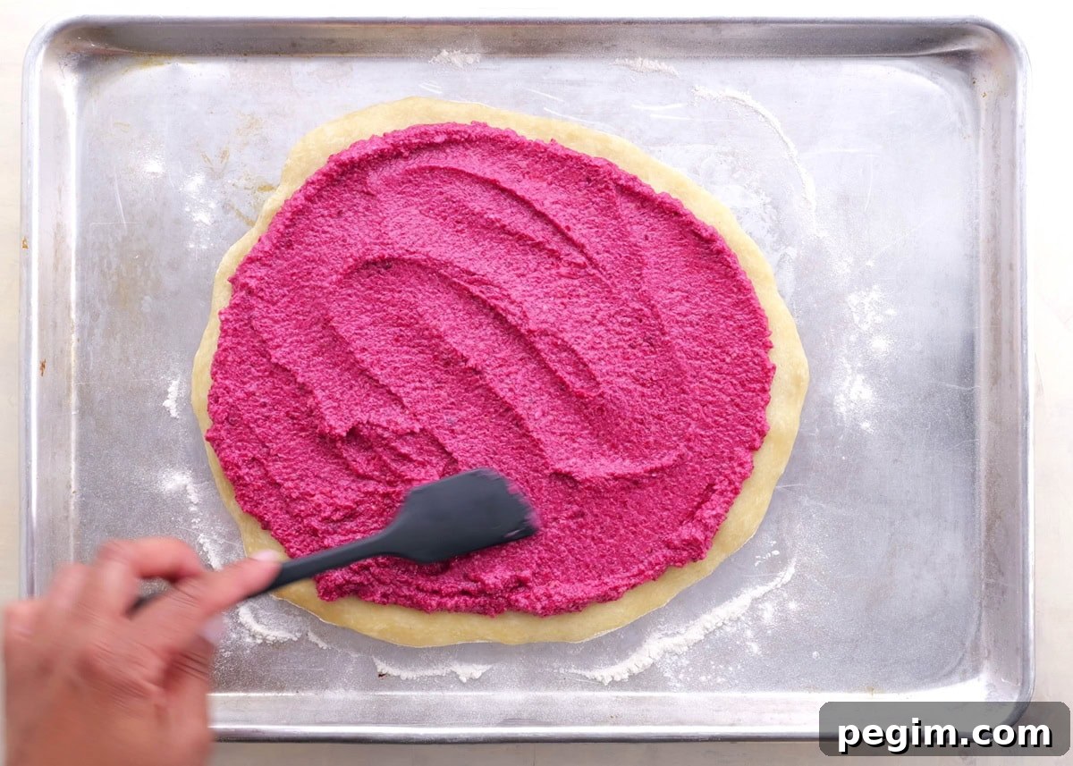 Hand spreading beet pesto over pre-baked pizza crust.