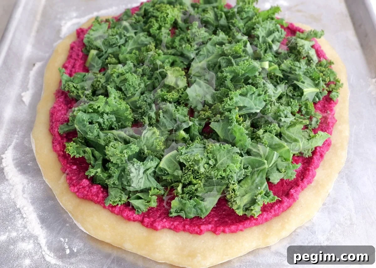 Pizza crust with beet pesto and chopped kale on top.