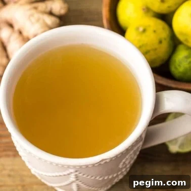A mug of fresh ginger drink with some ginger and key limes on the side