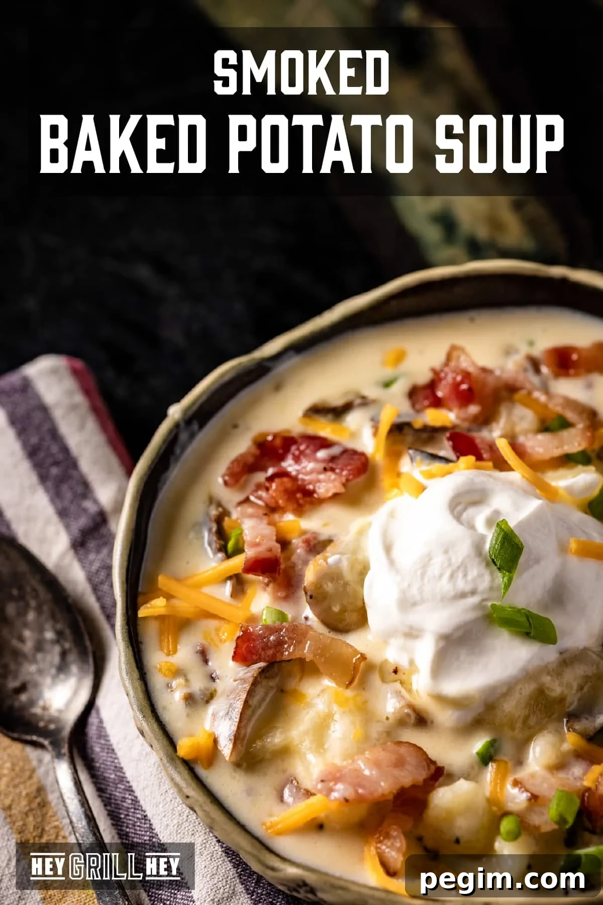 A closeup shot of a bowl of soup topped with shredded cheese, bacon bits, and a dollop of sour cream. The text overlay reads "Smoked Baked Potato Soup" at the top, and "Hey Grill Hey" at the bottom.