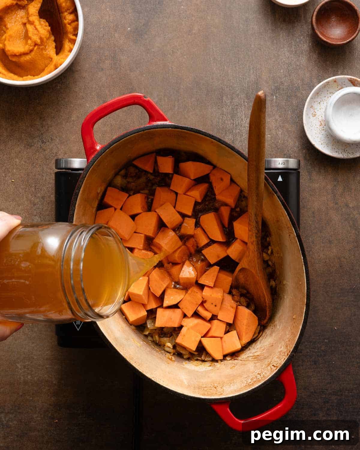 broth and sweet potato cubes being added to pot on burner.