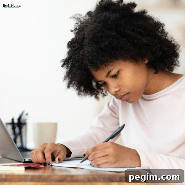 A student focused on writing an essay while studying with a laptop.