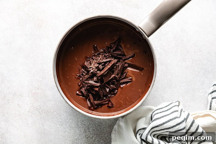 Finely chopped chocolate being added to a saucepan of warm pudding mixture.