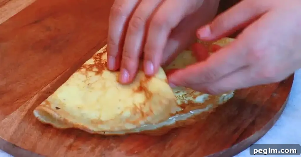 folding a crepe filled with whipped cream and strawberries