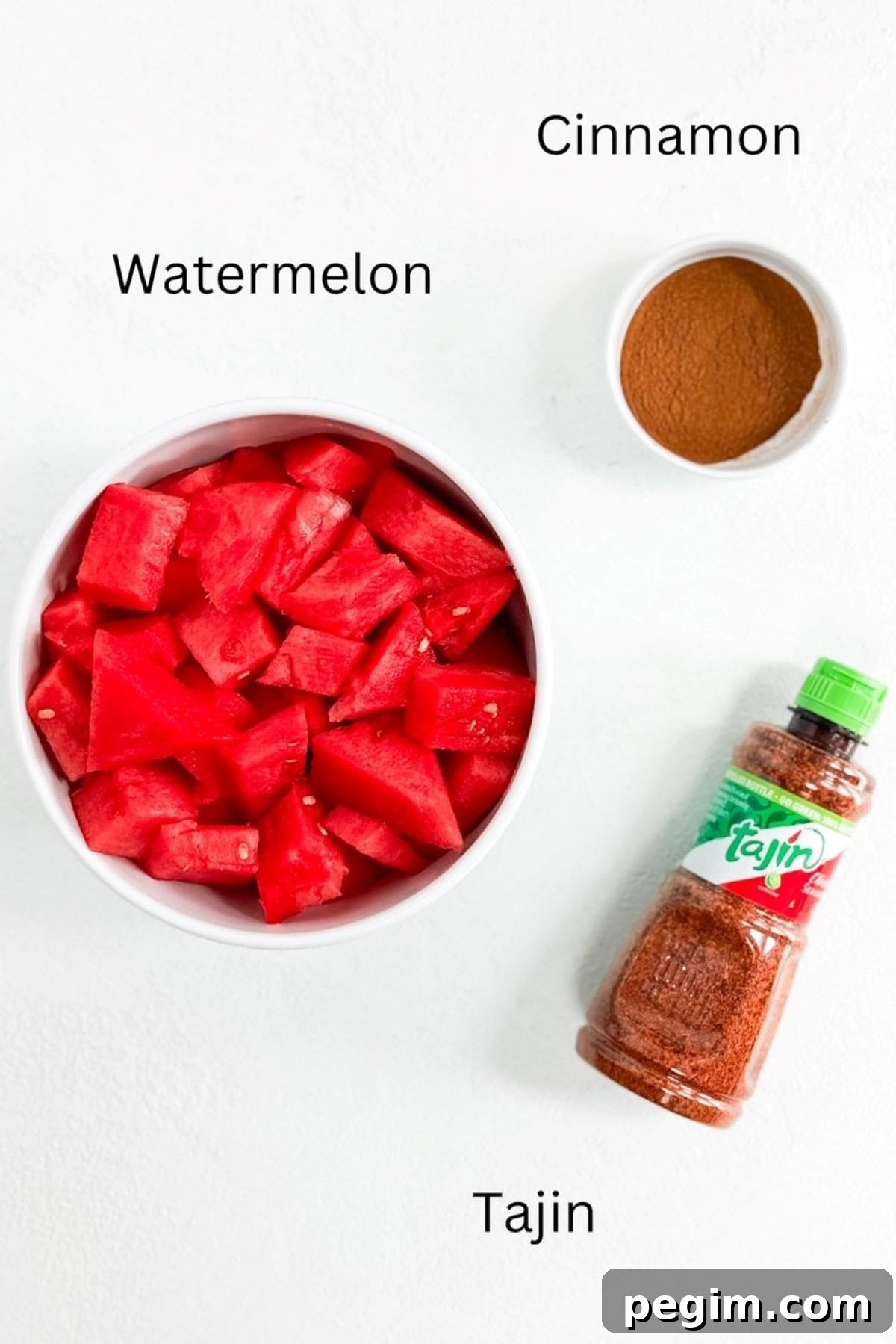 Watermelon in a bowl, cinnamon in a small bowl, and a bottle of Tajin.