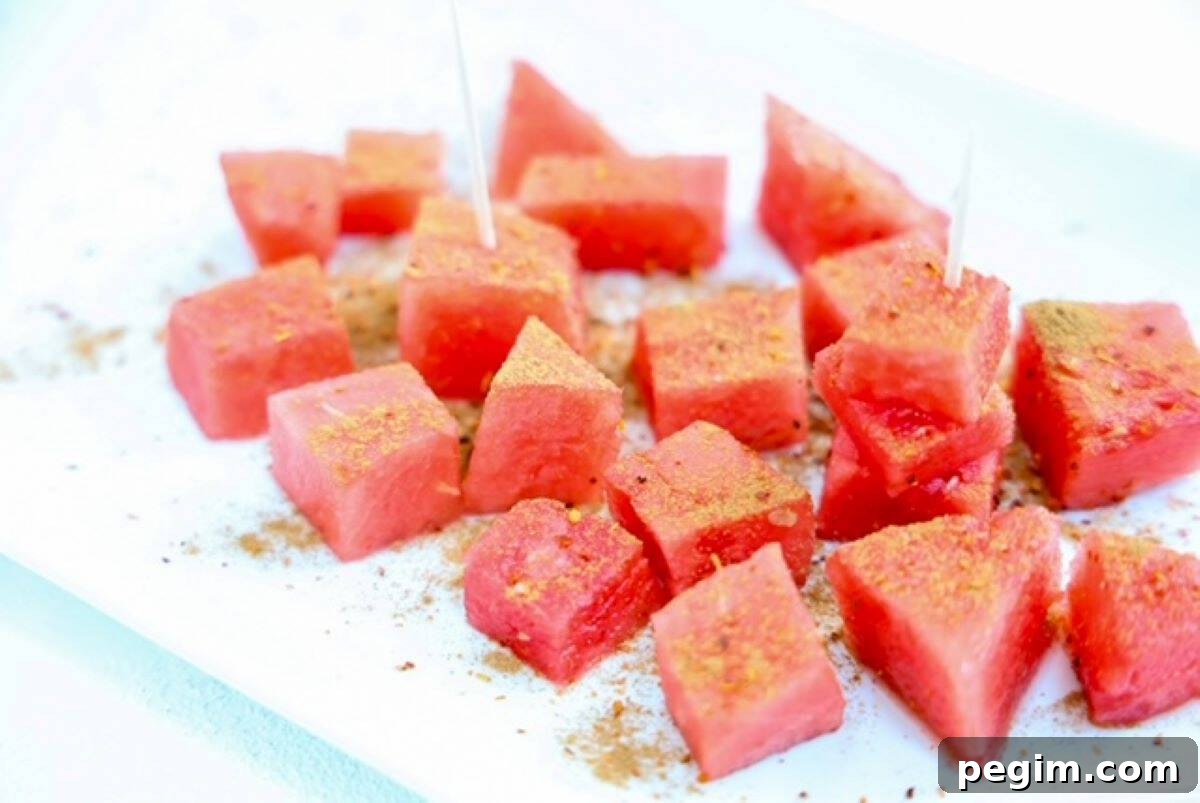 Watermelon topped with seasonings on a white plate.