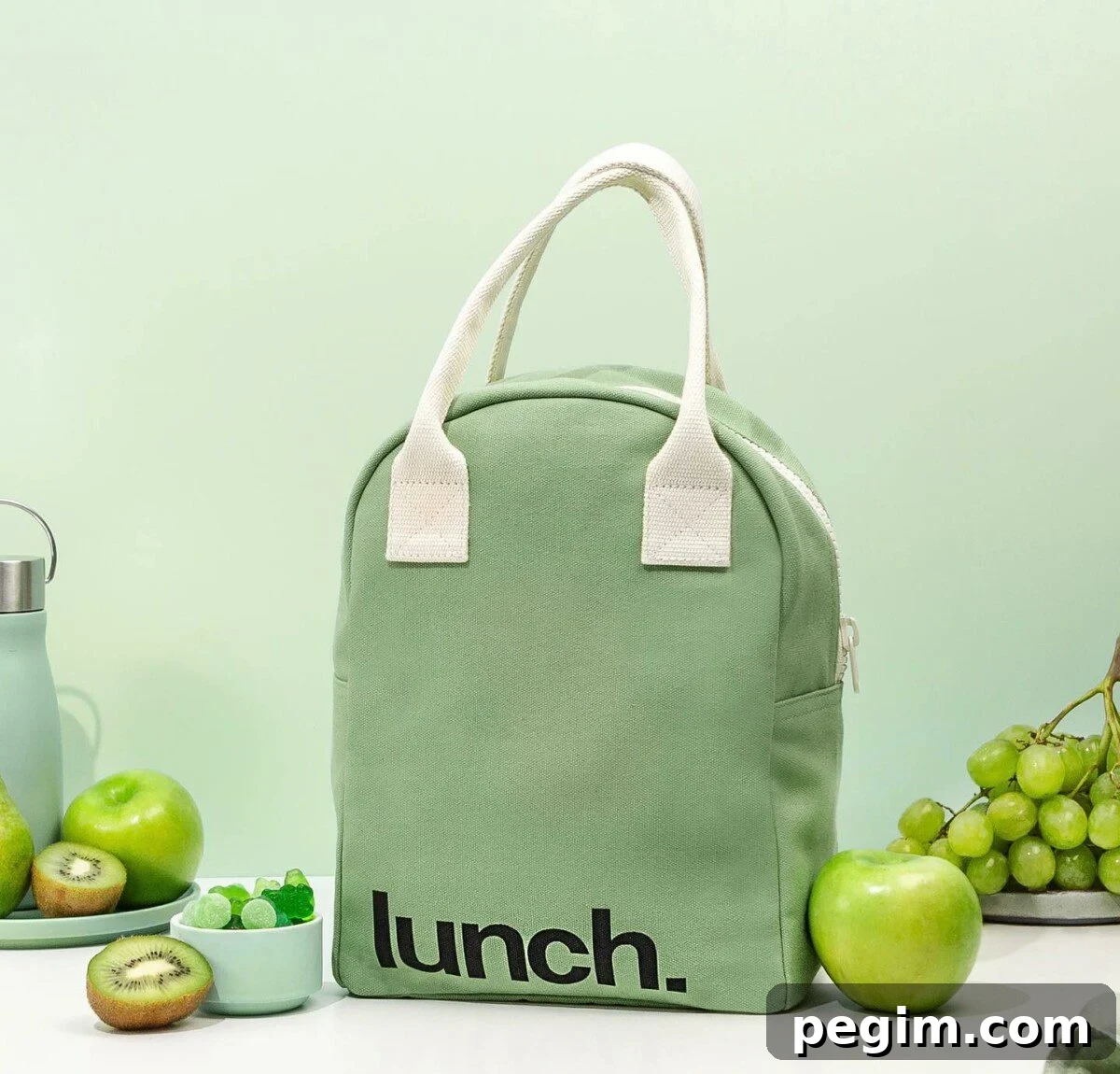 A mint-colored, eco-friendly organic lunch bag for adults by Fluf, accompanied by fresh green apples, kiwi, grapes, and a bowl of gummies