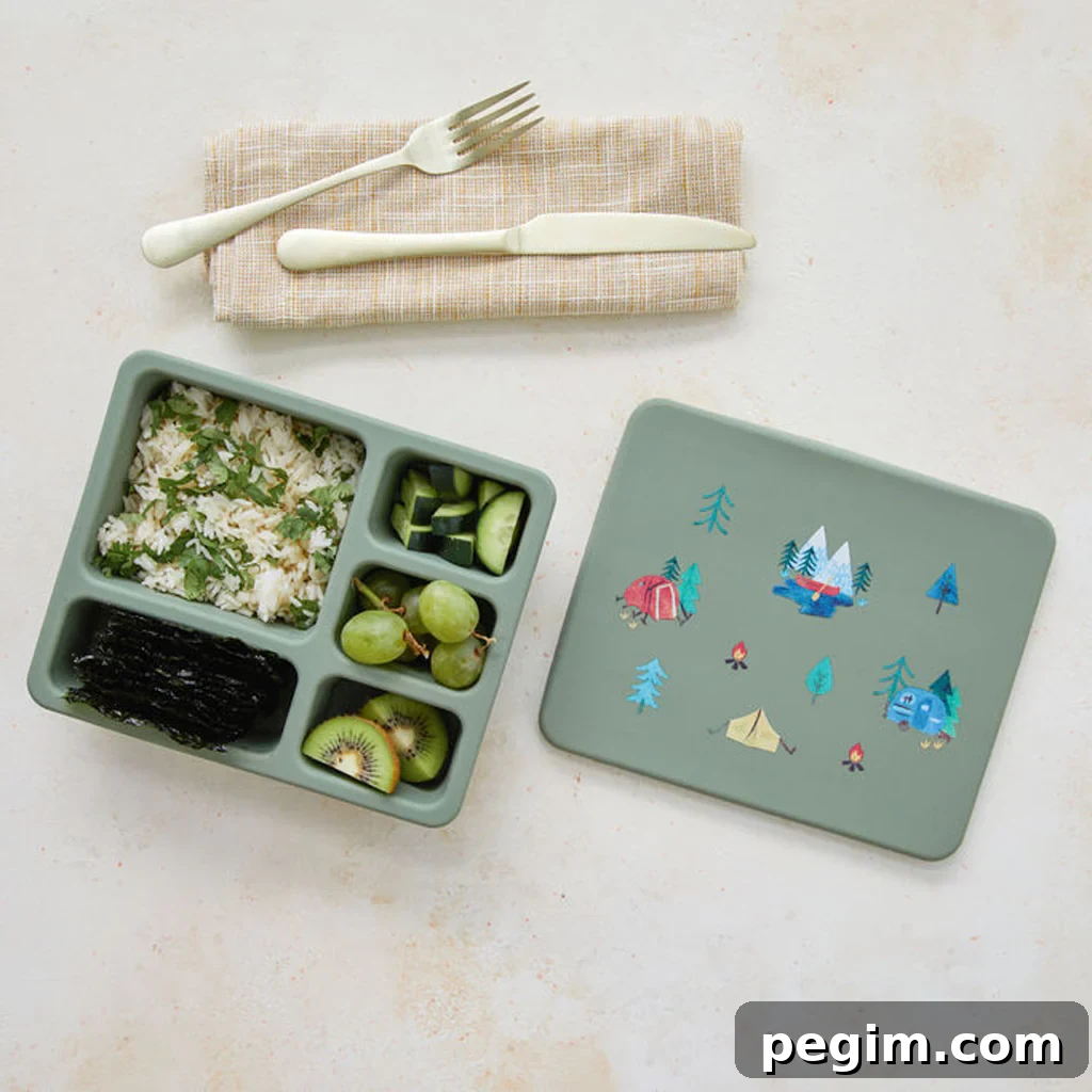 An Austin Baby Collection silicone bento box, opened to show rice, veggies, and fruits, with a knife, fork, and tissue placed next to it.
