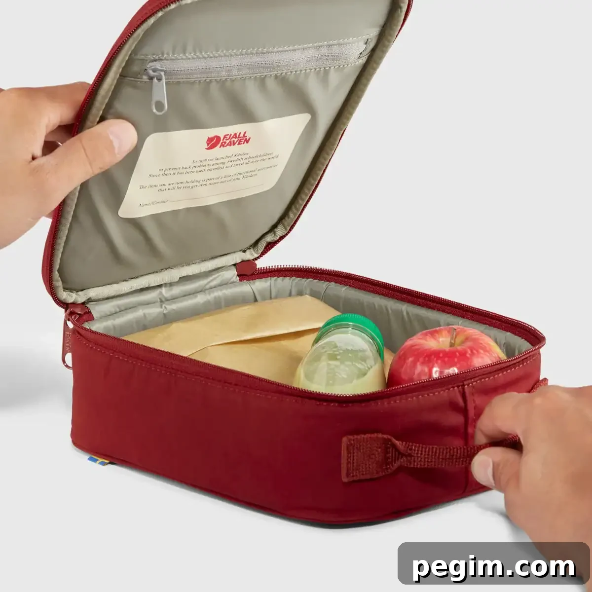 The maroon Kanken Mini Cooler by Fjällräven, with a drink and apple inside, fully opened.