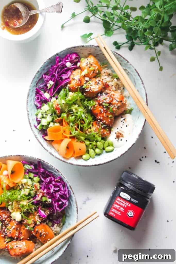Two baked salmon poke bowls on a marble background with honey on the side.