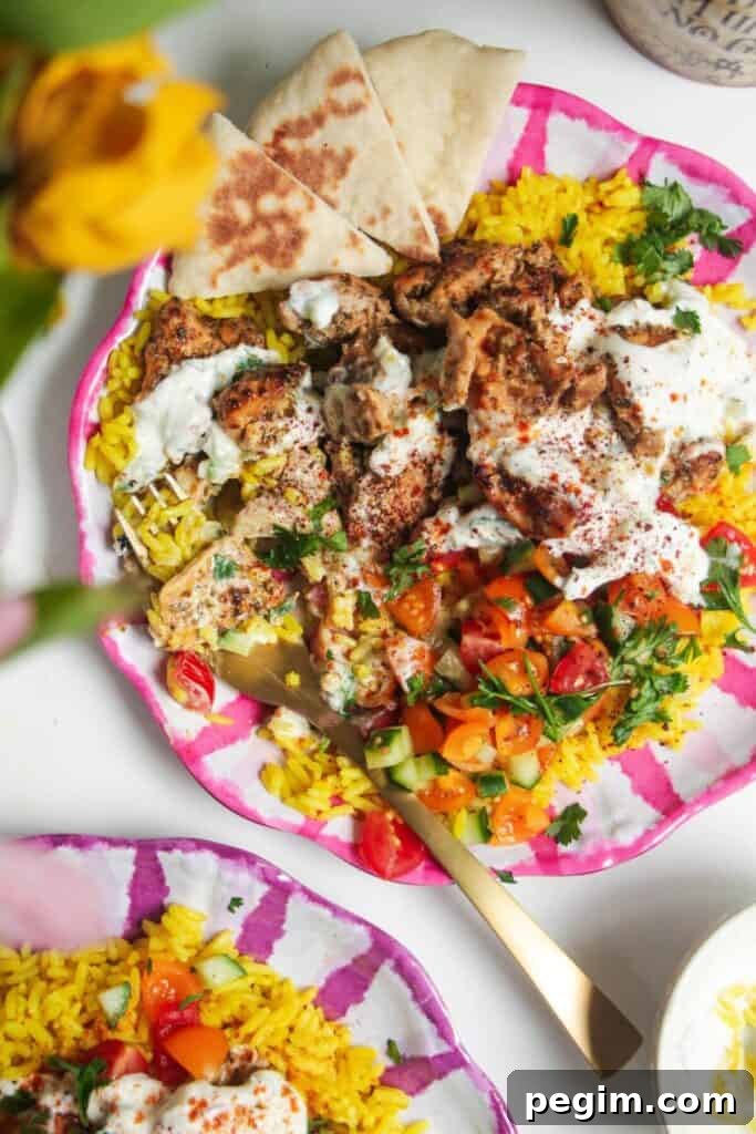 Chicken, salad and rice on a pink and white striped plate with pita bread on the side.