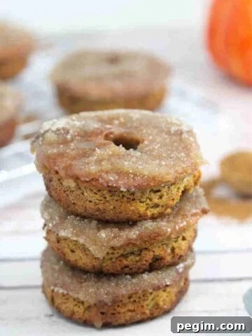 Three gluten-free pumpkin donuts stacked on top of one another with more donuts in the background.