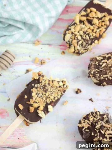 Chocolate coated ice cream bars with peanuts on parchment paper with one having a bite out of it.