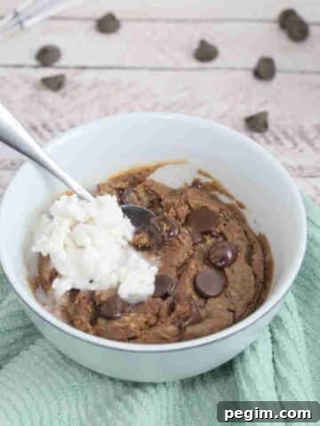 Chocolate brownie with chocolate chips in a white ramekin with coconut whip cream on top and a spoon in it.