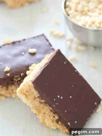 Two squares of protein rice krispies topped with chocolate leaning on each other and more in the background.