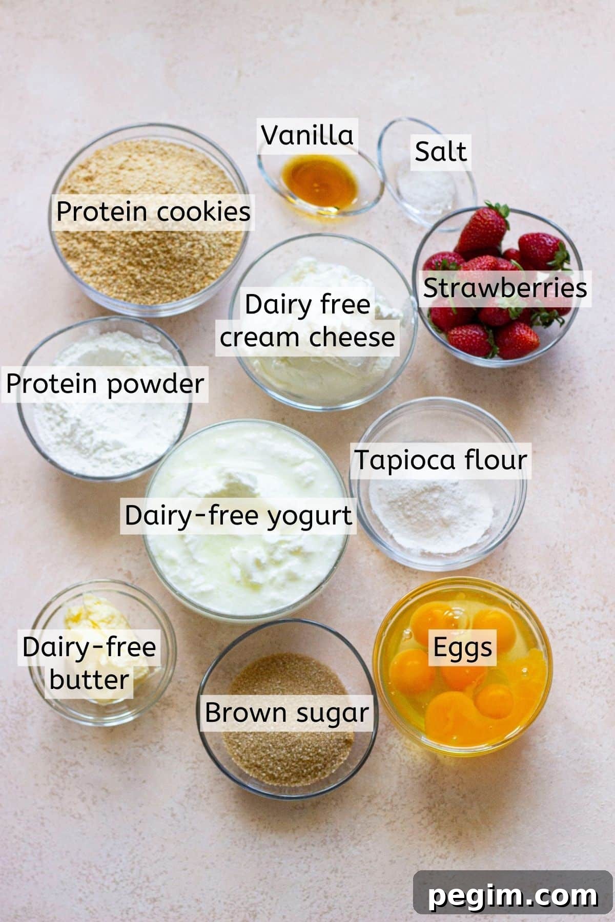 Ingredients to make protein cheesecake in measuring bowls with text labels over top.