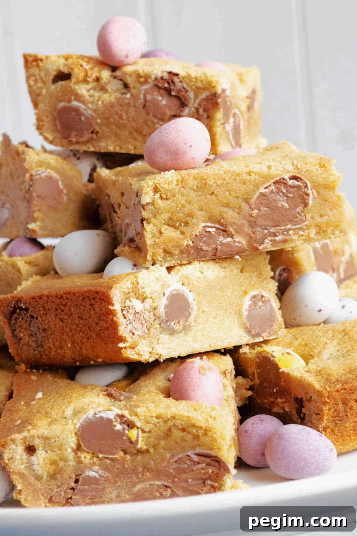 Mini egg cookie bars stacked on a cake stand with extra mini eggs for decoration.